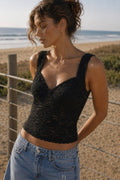 Woman wearing a black top and blue jeans standing on a beach.