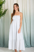 Woman wearing a light blue striped tiered maxi dress featuring a smocked bodice, spaghetti straps, and a breezy ankle-length silhouette for spring and summer against a light curtain background