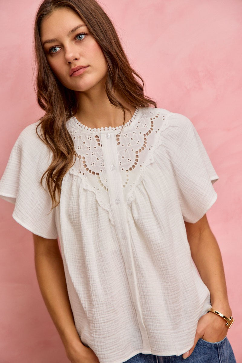 Women’s white ivory cotton blouse with lace yoke detail, short sleeves, button front, and relaxed boho fit against a pink background 