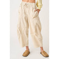 Close-up shot from image_5.png showcasing a woman modeling slouchy, high-waisted cotton cargo trousers in a sand hue, with heavy panel detailing, deep side pockets, and an elastic gathered waist worn by a person on a white background
