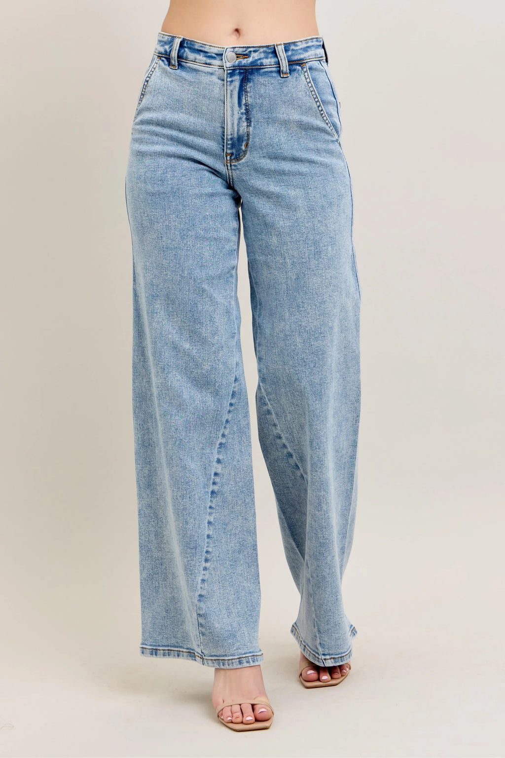 Front view of a person wearing high-waisted, light-wash wide-leg denim jeans with unique diagonal seam detailing and a relaxed fit on a beige background.
