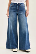 Front view of medium-wash, high-waisted wide-leg jeans with a floor-length hem, classic five-pocket styling, and subtle whiskering at the hips with white loafer shoes on a plain background 