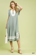 Flowy and cotton blend mint colored midi dress with cream contrast trim, flutter sleeves, side pockets, and side slit detail in a relaxed coastal-inspired silhouette. Woman wearing a light green dress with white accents on a light green background