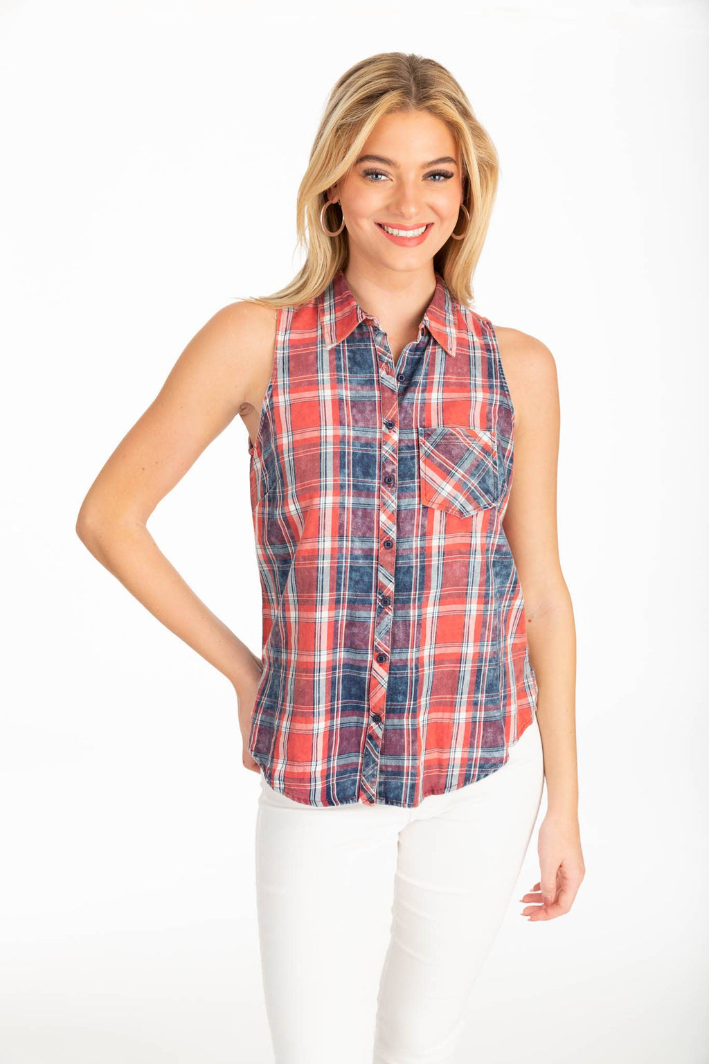 A woman smiling in a sleeveless red, blue, and white plaid button-down shirt with a single chest pocket, paired with white pants on a white background