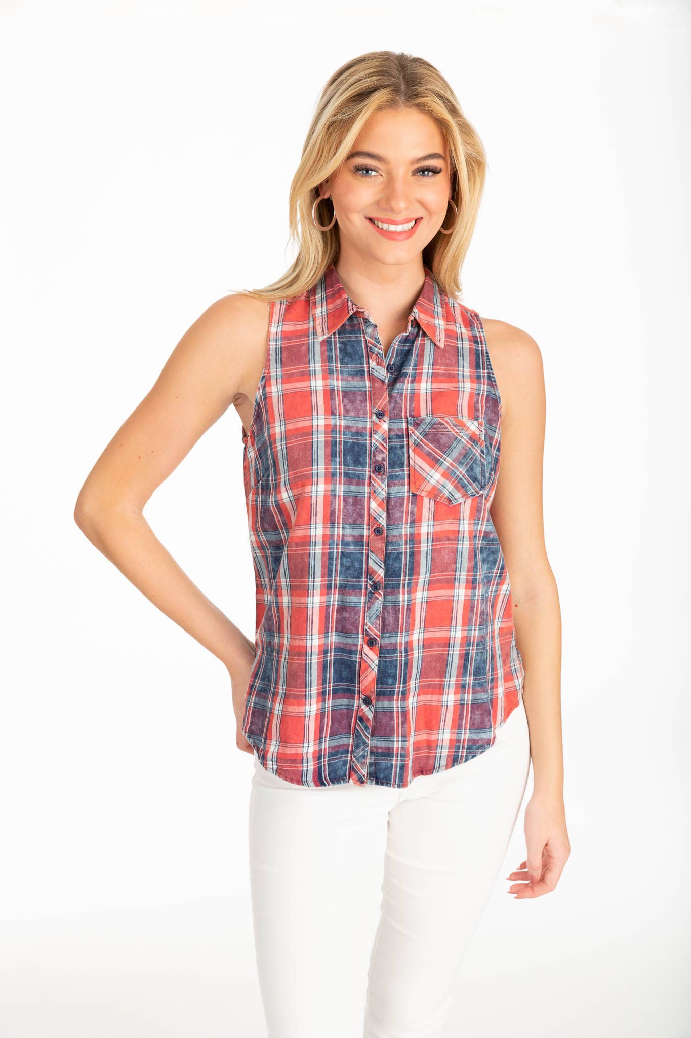 A woman smiling in a sleeveless red, blue, and white plaid button-down shirt with a single chest pocket, paired with white pants on a white background