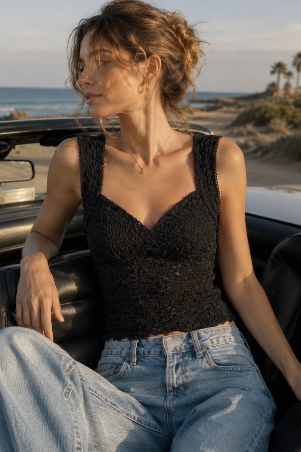Woman sitting in a convertible car by the beach
